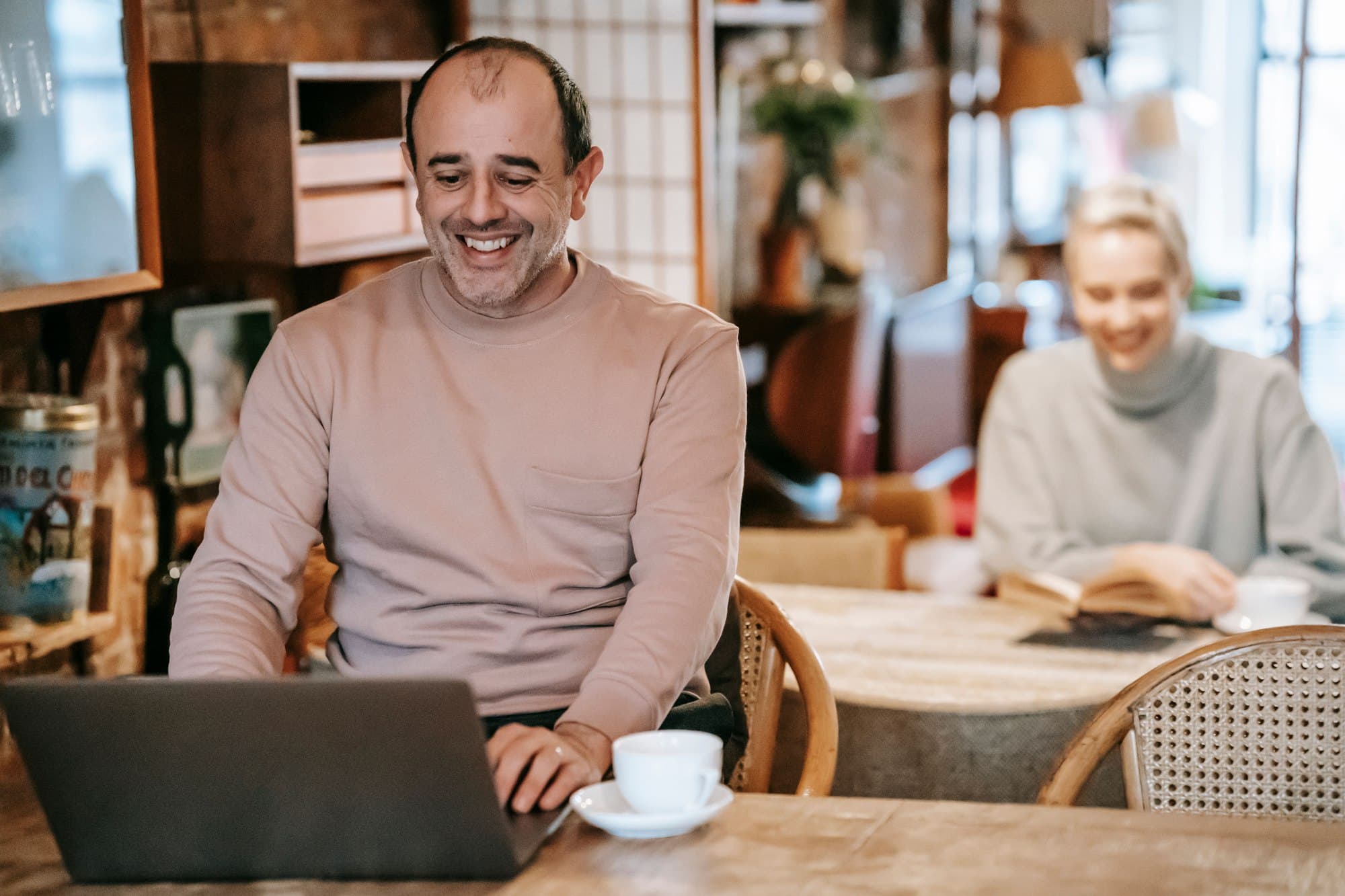 Un homme souriant devant son ordinateur portable, un café à la main